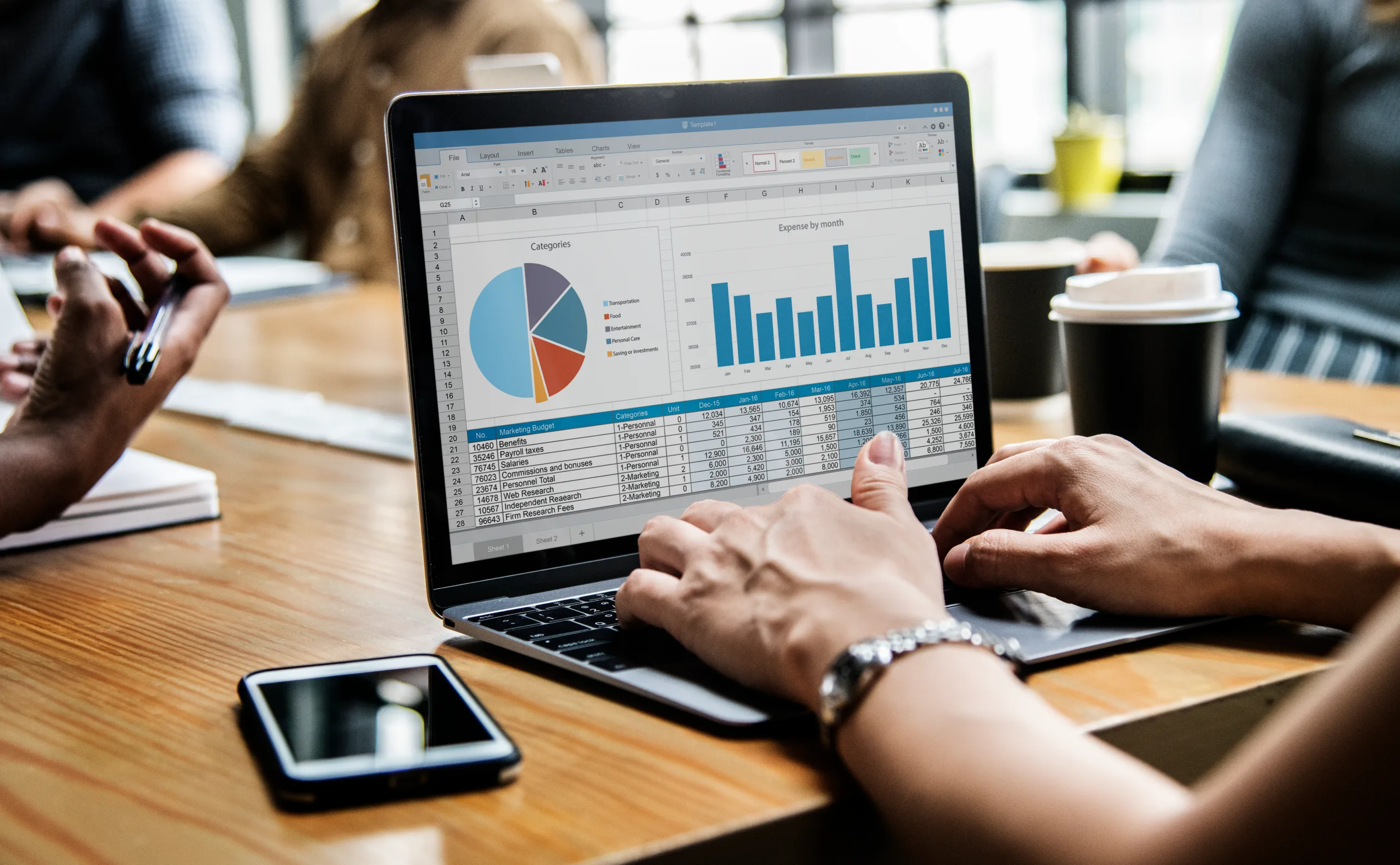 Close-up view of hands working on a laptop displaying pie and bar charts with financial data, during a business meeting at a wooden table.